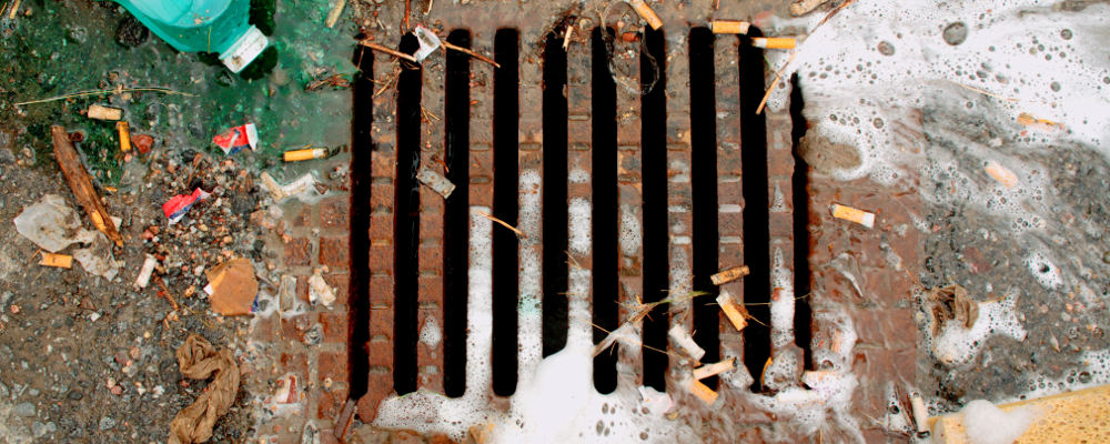 En gatubrunn med skräp, tvättskum och kemikalier runt.