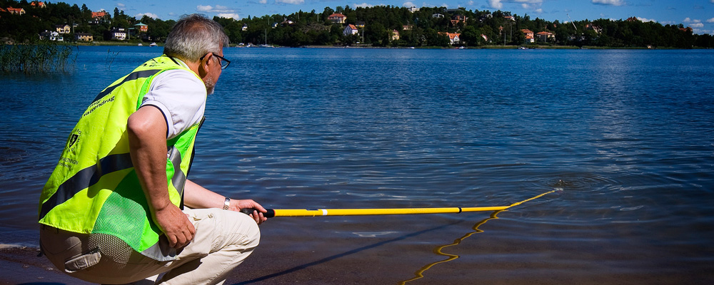 Personal från staden tar ett vattnprov i strandkanten